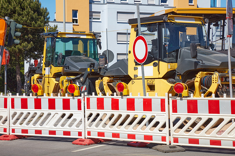 Absperrbaken mit Warnleuchten vor Baumaschinen auf innerstädtischer Baustelle