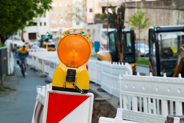 Warnbakenleuchte auf innerstädtischer Baustelle mit Absperrung und Radfahrer im Hintergrund